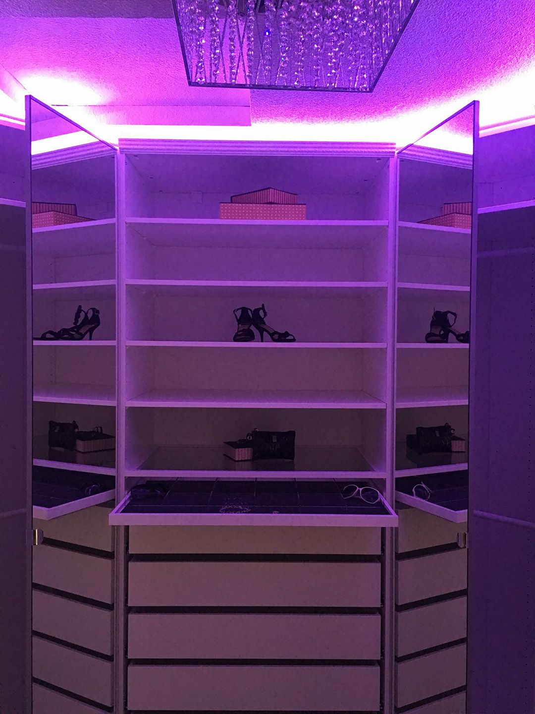 Custom closet with drawer storage, open shelving, and chandelier lighting.